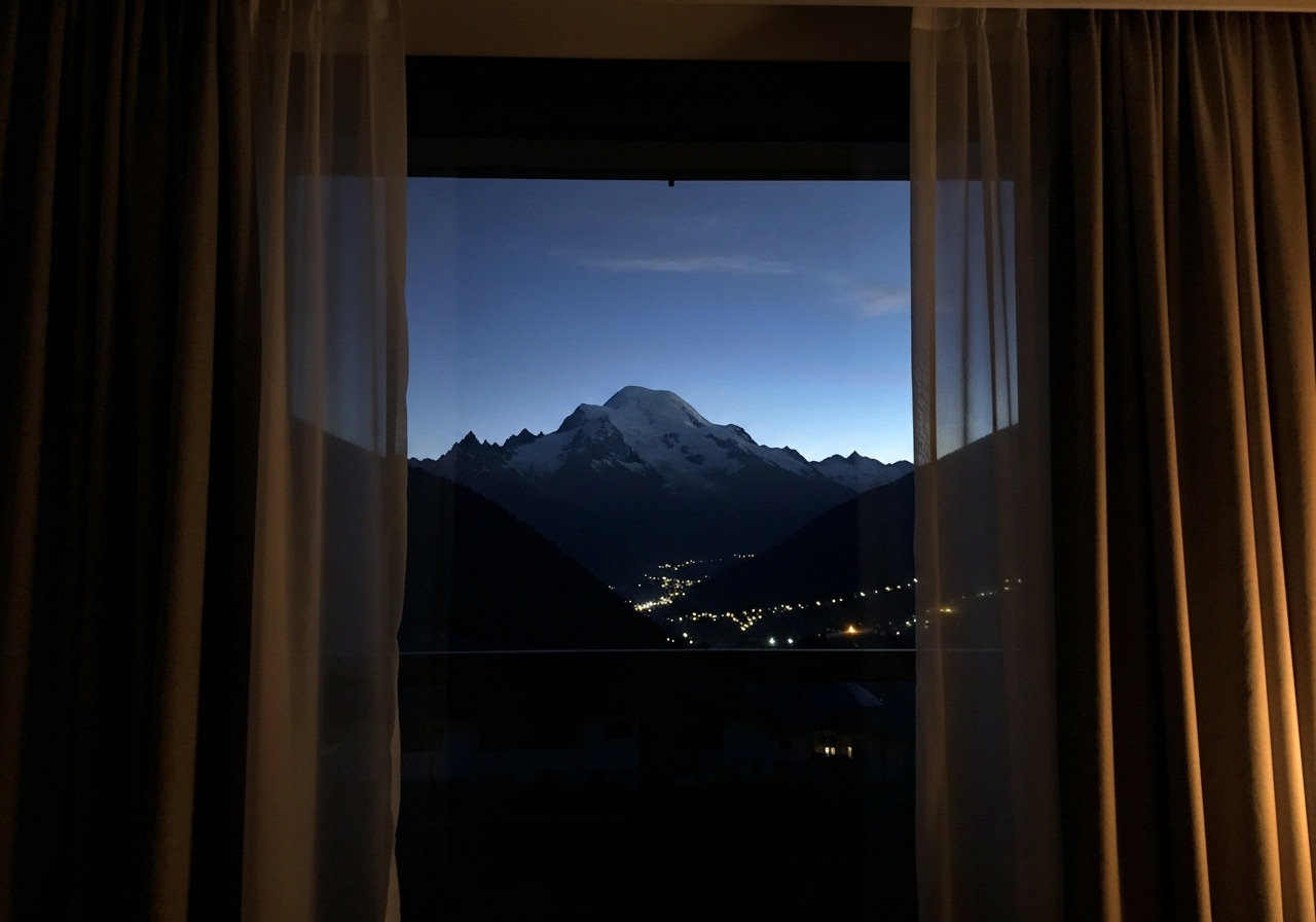 Hotel room window view at night, curtains partially drawn, showing the shadowy silhouette of Mont Blanc against a dark sky, faint valley lights visible below, intimate and contemplative atmosphere, authentic smartphone photo quality