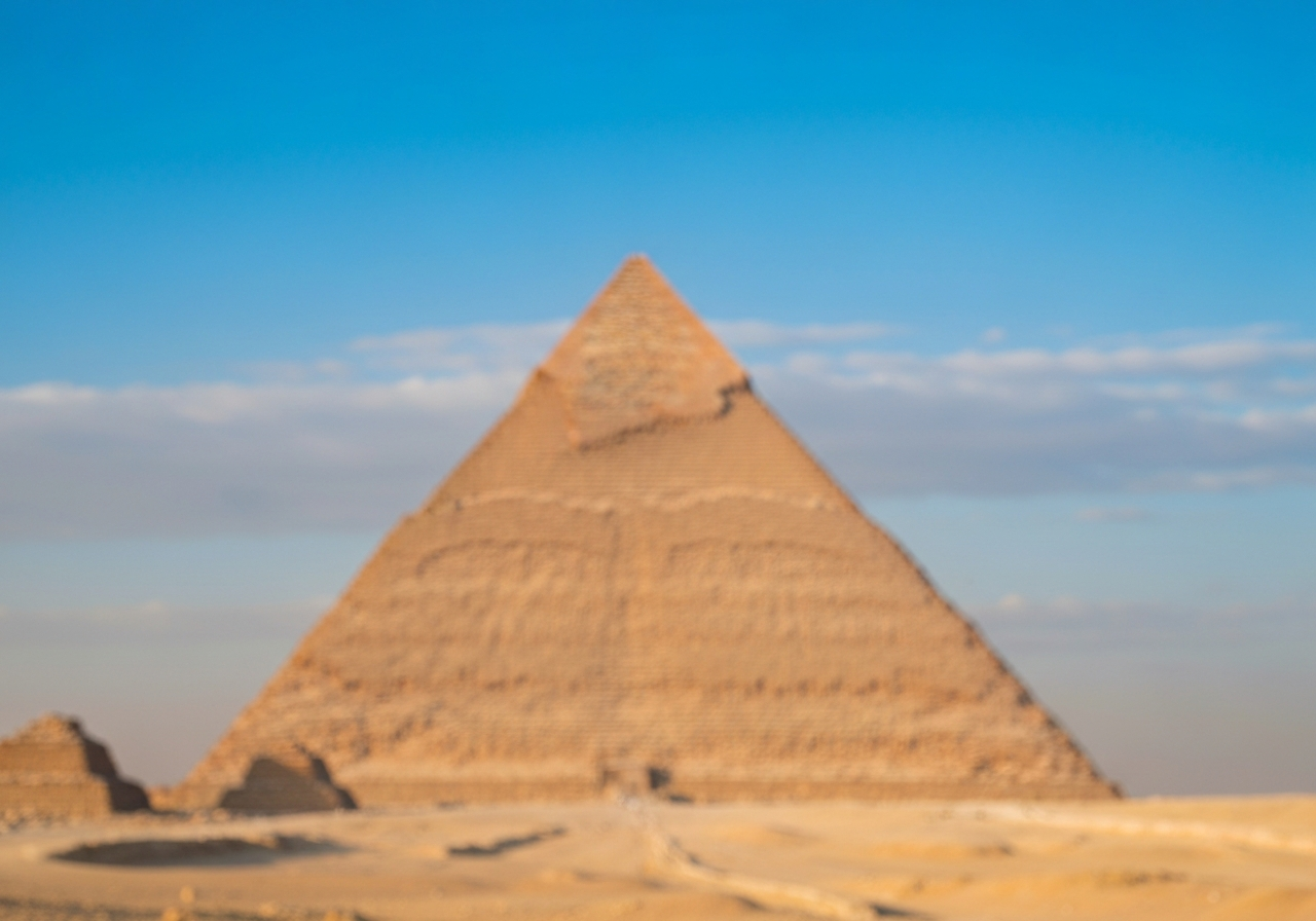 A slightly blurry, handheld shot from a smartphone taken at dawn, showing the immense scale of the Great Pyramid of Giza. The sky is a soft gradient of pre-sunrise colors, and there are only a few distant figures, emphasizing solitude. The focus is on the texture of the ancient stone blocks